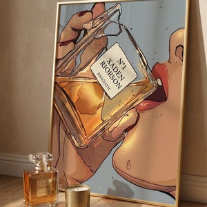 Pode incluir: Uma impress&atilde;o art&iacute;stica emoldurada com uma pessoa bebendo de um frasco de perfume. O frasco tem um r&oacute;tulo que diz "N&deg;1 Xaden Riorso Basgiath". Um frasco de perfume e uma vela dourada est&atilde;o em frente &agrave; impress&atilde;o.