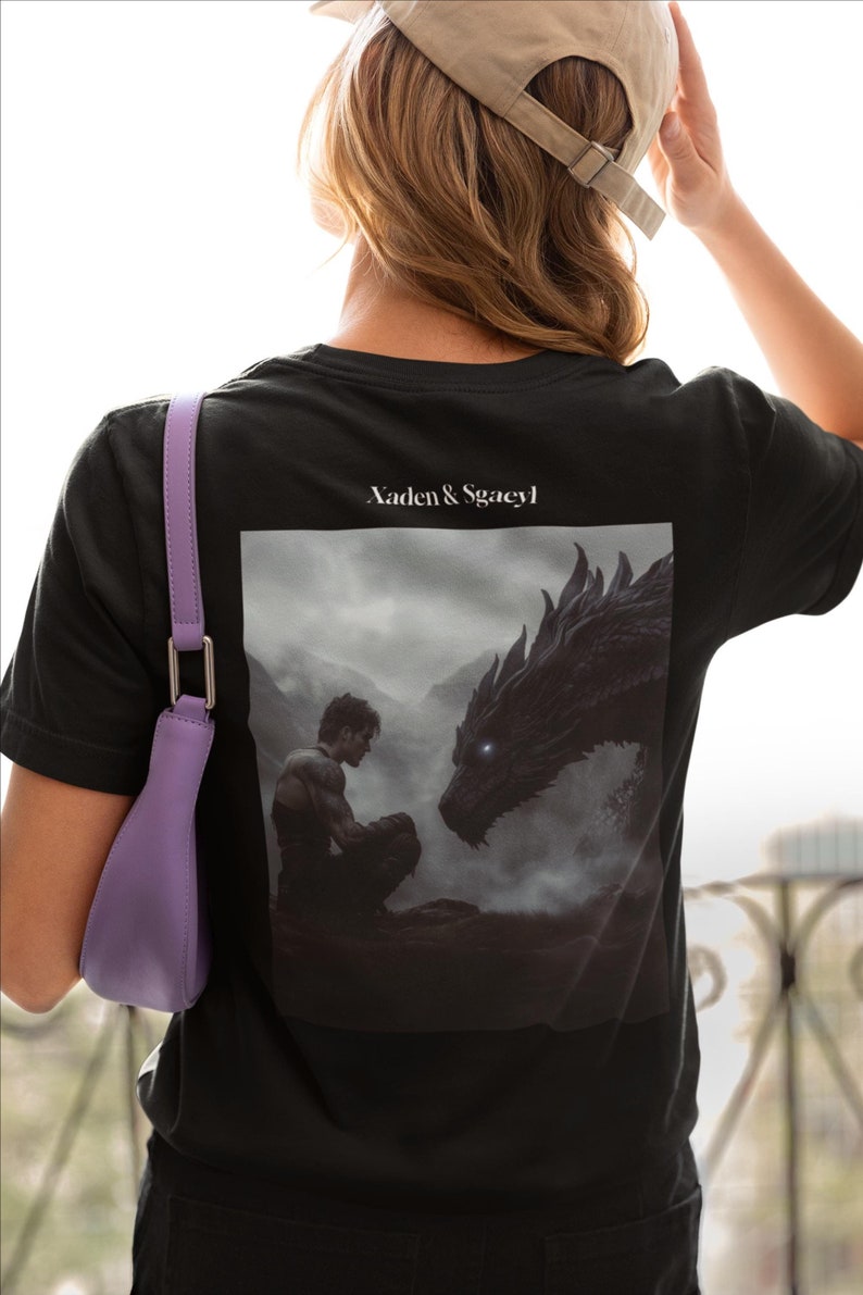 May include: Black t-shirt with a graphic print of a man and a dragon. The text "Xaden & Sgacy" is printed on the shirt.
