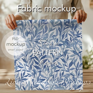 Könnte beinhalten: Ein Stoff-Mockup mit einem blauen und weißen Blumenmuster. Der Text "Your Pattern Here" ist auf dem Stoff geschrieben. Der Stoff wird von den Händen einer Person gehalten.