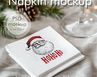 May include: A white napkin mockup with a hand-drawn illustration of Santa Claus with the text "HOHOHO" in red. The napkin is folded in half and has a subtle texture. The image is set against a light gray background.