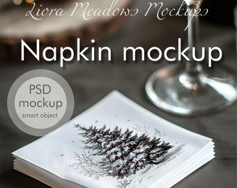 May include: A white napkin with a wintery design of a snow-covered tree with red berries. The napkin is folded and placed on a dark gray surface. The text "Napkin mockup" is written in white on a dark gray background. The text "PSD mockup smart object" is written in white on a circle with a gray background.