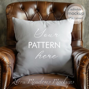 May include: A gray throw pillow with the text "Your Pattern Here" on a brown leather armchair.