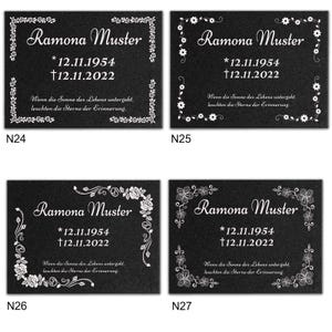 May include: Four black granite memorial plaques with white floral borders and text. The text reads "Ramona Muster *12.11.1954 &dagger;12.11.2022" and "Wenn die Sonne des Lebens untergeht, leuchten die Sterne der Erinnerung."