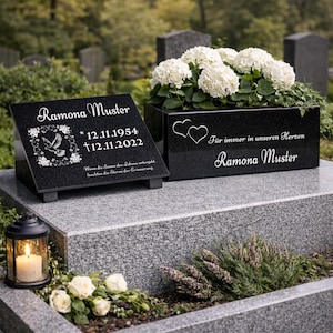 Könnte beinhalten: Ein schwarzes Granitdenkmal mit dem Namen "Ramona Muster" und den Daten 12.11.1954 - 12.11.2022. Ein Tauben- und Blumendesign befindet sich links. Ein rechteckiger Pflanzkübel mit weißen Blumen und dem Text "Für immer in unseren Herzen" befindet sich rechts.
