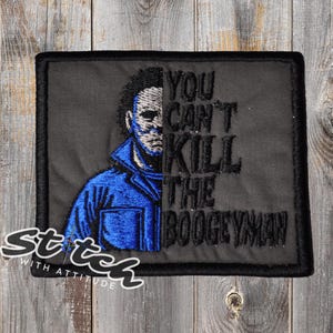 May include: Embroidered patch featuring a split image of a character in a blue jumpsuit and the text "YOU CAN'T KILL THE BOOGEYMAN." The patch has a black border and is set against a wooden background. The words "Stitch with Attitude" are also in the image.