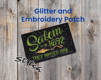 May include: Black glitter and embroidered patch with the text "Salem *1692 THEY MISSED ONE" in green and gold. The patch is rectangular and has a black border. The words "Glitter and Embroidery Patch" are above the patch.