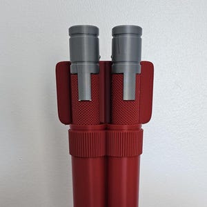 May include: A pair of red and grey double-barreled blasters with a textured surface. The blasters are in a red holster.