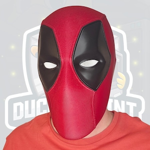 May include: A red Deadpool mask with black eye coverings and white mesh eye openings. The mask is made of a textured material and covers the entire head. The person wearing the mask is wearing a red shirt.