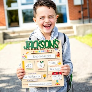 以下が含まれることがあります： 緑色の文字でJacksonと書かれた木製の初登校日用ボード。学年、身長、年齢、好きな色、先生の名前、将来の夢、日付を記入する欄があり、鉛筆やリンゴなどのカラフルなアイコンが描かれています。