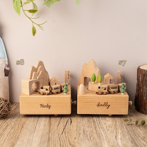 May include: Two wooden music boxes with personalized names "Hedy" and "Sally". Each box features a miniature train traveling through a mountain scene with a tunnel and trees.