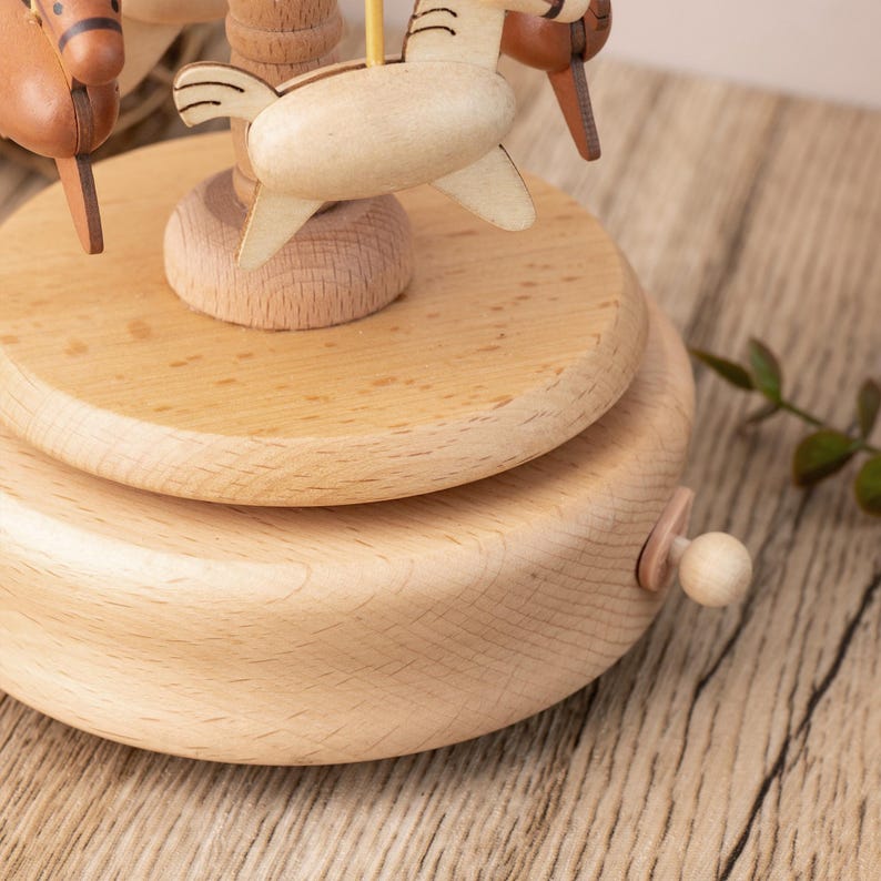 May include: A wooden music box with a carousel design. The carousel features three wooden horses with painted details. The music box has a crank on the side to wind it up.