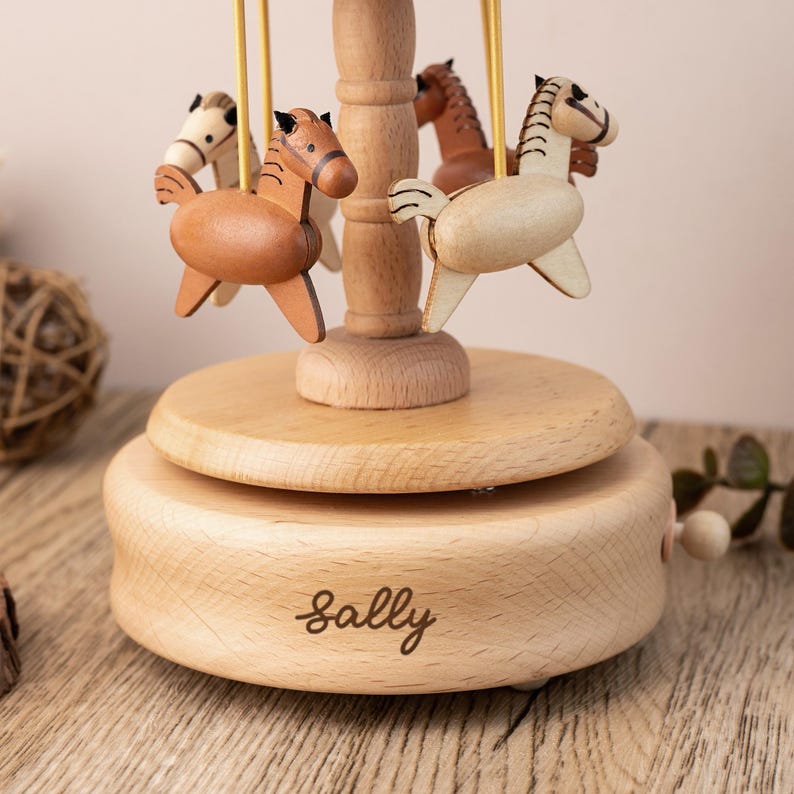 May include: A wooden carousel music box with a rotating platform and four wooden horses. The music box is personalized with the name "Sally".