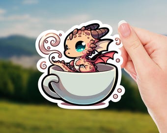 May include: A sticker featuring a cartoon dragon in a teacup. The dragon is peach-colored with red wings and big blue eyes. The teacup is white, and steam curls up from the cup. The sticker is held by a hand.
