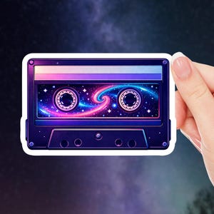 May include: A sticker featuring a retro cassette tape design. The tape is dark blue with a white border and a cosmic galaxy design inside, with pink, blue, and purple hues. The sticker is held by a hand against a dark, starry background.