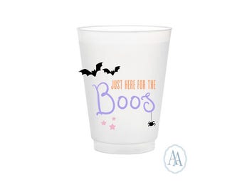 Pode incluir: Um copo de plástico branco com o texto "Just Here For The Boos" em roxo e laranja. A caneca é decorada com morcegos pretos, estrelas cor-de-rosa e uma aranha, perfeito para o Halloween.