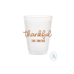 May include: A white plastic cup with the word "thankful" in a brown script font. Below the word "thankful" is the text "THE SMITHS" in a smaller, blocky brown font. A small, circular logo is in the bottom right corner.