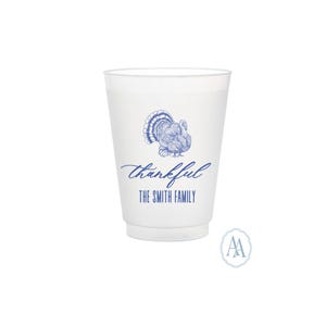 May include: A white plastic cup with a blue turkey illustration and the word "thankful" in script. Below the word "thankful" is the text "THE SMITH FAMILY". The cup has a frosted appearance and is likely for a special event.