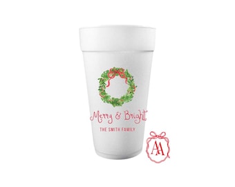 May include: White foam cup featuring a Christmas wreath design. The wreath is green with red ribbon. The words "Merry & Bright" are written in red script, along with "THE SMITH FAMILY". A red bow logo is also visible.