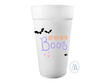 Pode incluir: Um copo de espuma branco com o texto "Just Here for the Boos" em roxo e laranja. O copo é decorado com morcegos pretos, estrelas cor-de-rosa e uma aranha. É um item com tema de Halloween.