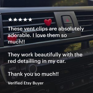 May include: Two red heart-shaped vent clips installed in a car's air vent. The car's interior is black. Text on the image says, "These vent clips are absolutely adorable. I love them so much!!" and "Thank you so much!!"