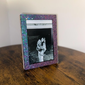 May include: A picture frame with a black and white photo of two people. The frame is decorated with iridescent rhinestones.