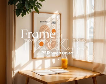 Könnte beinhalten: Ein gerahmter Druck mit einem geometrischen Design in Orange und Weiß mit dem Text "Bauhaus Exhibition 1923" auf einem Holztisch neben einer Glasflasche Orangensaft. Der Druck ist in einem Holzrahmen und der Tisch ist aus Holz.