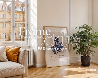May include: A gold frame mockup with a white background and a blue and white abstract design. The frame is hanging on a white wall in a living room setting with a couch, a plant, and a window.