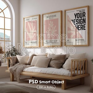 Op de afbeelding: Een mockup van drie ingelijste kunstprints met een lichtroze achtergrond en abstracte vormen. De lijsten zijn van hout en hebben een witte passe-partout. De prints hangen aan een witte muur boven een houten bank met kussens. De tekst op de prints luidt "Matisse", "Uw ontwerp hier" en "Belcgruen & Cie".