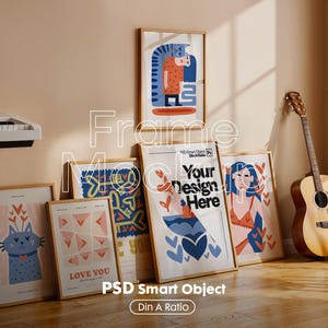 May include: A collection of framed art prints with various designs, including a cat, abstract shapes, and figures. The frames are wooden, and the prints are displayed against a neutral wall. Text on the prints includes "LOVE YOU" and "Your Design Here". A guitar leans against the wall.