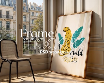 May include: A framed print with a yellow cheetah illustration and green tropical leaves. The text "wild cute" is written below the cheetah. The frame is gold and the background is a light beige.