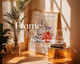May include: A gold frame mockup with a poster inside. The poster has a blue and red abstract design with the text "PAPIERS DÉCOUPÉS" and "MATISSE PARIS, FRANCE 1955". The frame is sitting on a table with a stack of books and a plant in a glass vase.