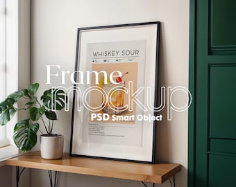 May include: A black framed poster with a white background and a recipe for a Whiskey Sour cocktail. The poster has a picture of a glass of whiskey sour with a cherry on top. The poster is hanging on a white wall above a wooden table with a green plant in a white pot.