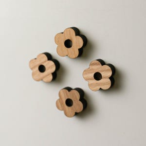 Puede incluir: Cuatro imanes de madera con forma de flor. Cada im&aacute;n tiene un dise&ntilde;o de flor marr&oacute;n claro con un borde marr&oacute;n oscuro y un agujero circular en el centro. Los imanes est&aacute;n dispuestos sobre una superficie blanca.