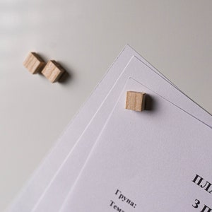 May include: Three wooden blocks are used to hold down a stack of white papers. The top paper has the text "План-конспект" and "3 Г" printed in black.