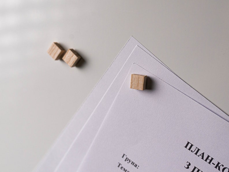 May include: Three wooden blocks are used to hold down a stack of white papers. The top paper has the text "План-конспект" and "3 Г" printed in black.