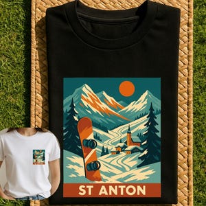 May include: Black t-shirt featuring a winter landscape with a snowboard and the text "ST ANTON". The design includes mountains, a church, and a setting sun. A smaller version of the design is on a white t-shirt.