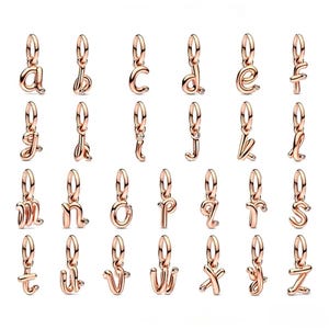 Puede incluir: Colección de colgantes de alfabeto en oro rosa, cada uno con una pequeña gema transparente. Los colgantes están en una fuente cursiva y están diseñados para ser utilizados como colgantes o adiciones a pulseras. Las letras son de la A a la Z.