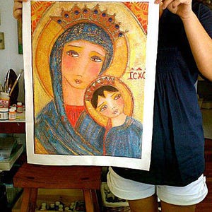 May include: A colorful religious icon print featuring the Virgin Mary and Child, both adorned with halos and crowns. The artwork has a gold background and is held up by a person. The image has the text "ICXC".
