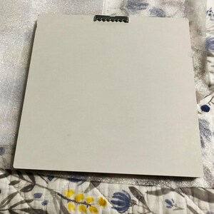 May include: A rectangular, off-white canvas with a metal sawtooth hanger attached to the top. The canvas is set against a patterned fabric background. The canvas is ready to be hung.