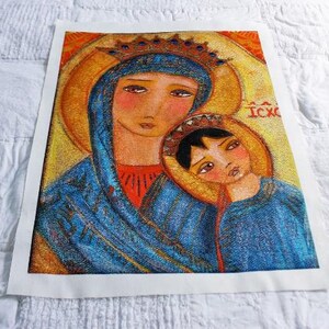 May include: A framed religious icon featuring a mother and child, rendered in a folk art style. The figures are depicted with soft features and are wearing blue and red garments. The background is gold with the Greek letters IC XC.