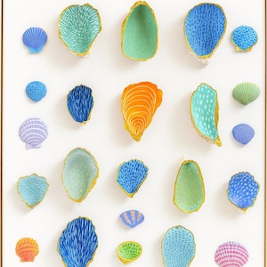 Puede incluir: Una obra de arte enmarcada con una colección de esculturas de conchas marinas coloridas y estilizadas. Las conchas están pintadas en tonos de azul, verde, naranja y rosa, con detalles dorados. La disposición está sobre un fondo blanco.