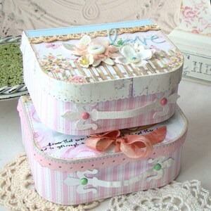 May include: Two pink and white striped boxes with a white handle and a pink bow. The top box has a floral design and the word "Love" written on it. The boxes are decorated with lace and glitter.