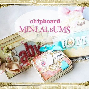 May include: A collection of handmade mini chipboard albums. The albums are decorated with floral accents, ribbons, and the words "Baby", "Home", and "kiss". The color palette includes pink, cream, and blue tones.