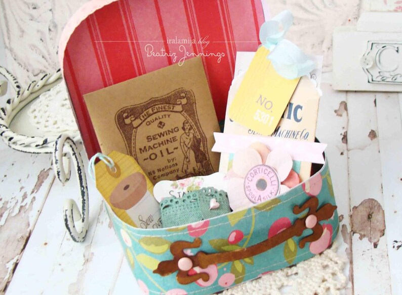 May include: A vintage-style floral fabric box with a brown handle and a metal clasp. The box is filled with various items, including a small sewing machine oil tin, a spool of thread, and several decorative tags. The text on the tags reads "No. 401", "Sewing Machine Co", and "The Finest Quality Sewing Machine Oil".