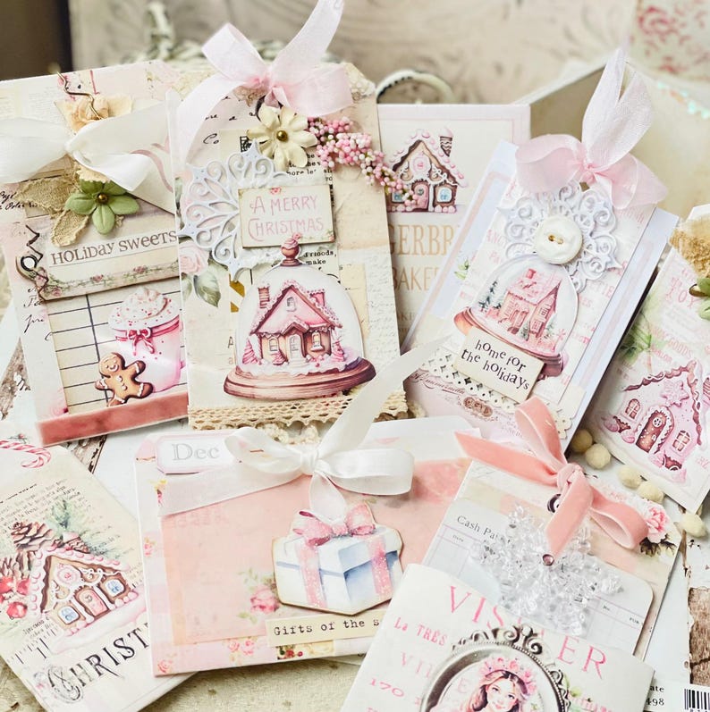 May include: A collection of handmade Christmas gift tags featuring pink and white paper, gingerbread houses, and festive text. The tags are decorated with ribbons, lace, and other embellishments.