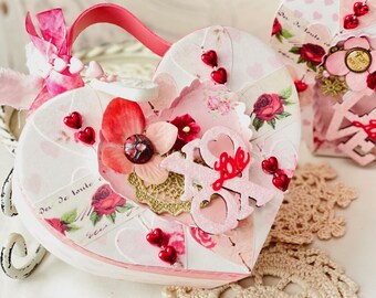May include: Two pink and white heart-shaped boxes decorated with red roses, hearts, and the word "Love". The boxes are adorned with red glitter and have a pink ribbon.