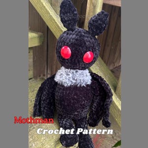 May include: A handmade black plush Mothman doll with red button eyes and a grey fur collar. The doll has large wings and is sitting on a wooden surface. The text "Mothman Crochet Pattern" is visible.