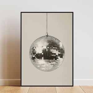 May include: A black and white photograph of a silver disco ball hanging from the ceiling against a light beige background.