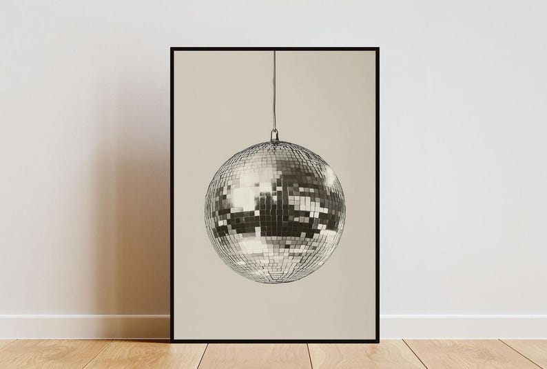 May include: A black and white photograph of a silver disco ball hanging from the ceiling against a light beige background.