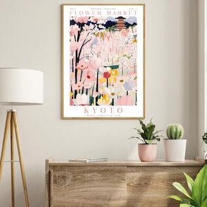 Op de afbeelding: Een vintage poster die reclame maakt voor een bloemenmarkt in Kyoto, Japan. De poster toont een kleurrijke illustratie van een bloemenmarkt met een pagode op de achtergrond. De tekst op de poster luidt "Bloemenmarkt, Kyoto, maandag - zondag 9:00 - 17:00".